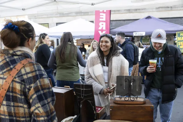 A man and woman visit a booth at a farmers market. 