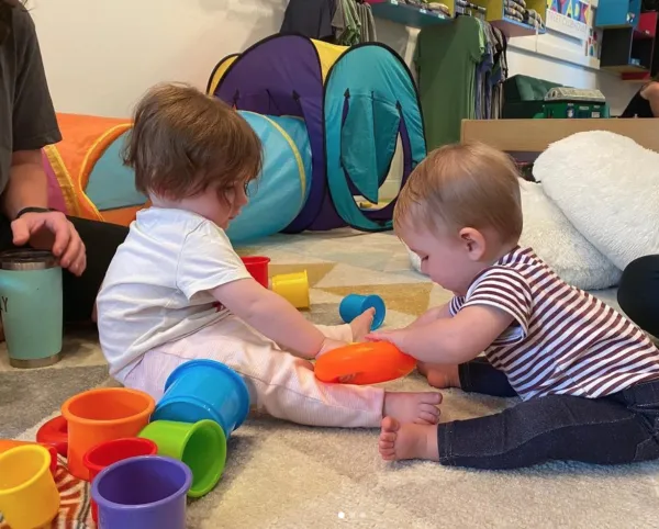 Babies sit and play with colorful stacking cups on a floor together