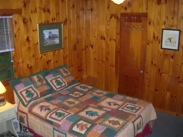 Pine tree themed quilt on a bed in a knotty pine panneled room.