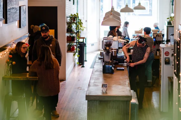 Barista prepares to pull a freshly ground espresso shot on a live edge bar while patrons mingle.