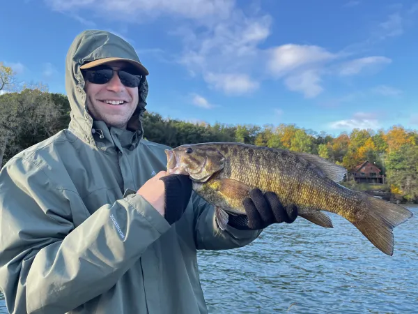 A man holding a fish smiles at the camera.