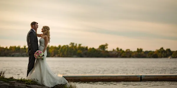 Bride and groom stand facing each other on the edge of a lake.