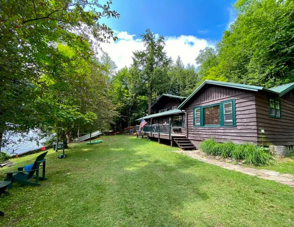 Lush green lawn next to blue waters of Lake Flower highlight the dark stain on this Log cabin by the lake.