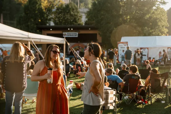 Women socialize surrounded by people in lawn chairs and at vendor booths