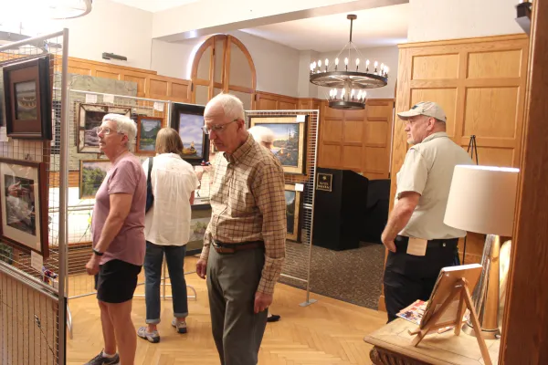 People observe the art inside a large room with wood paneled walls at the guide boat art show