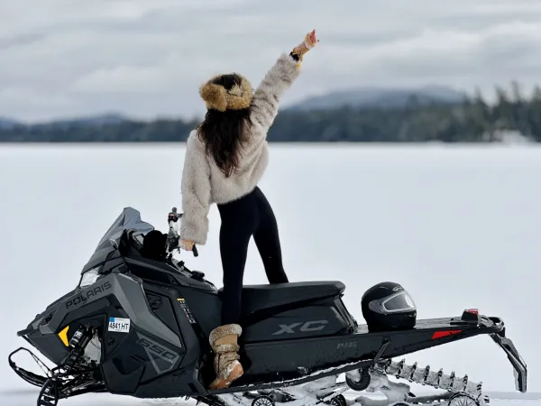excited girl in furs looks out over the snowy landscape a snow machine with mountain backdrop