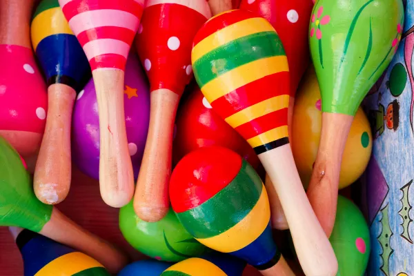 A vibrant, close-up overhead view of a pile of brightly colored, hand-painted wooden maracas featuring various patterns.