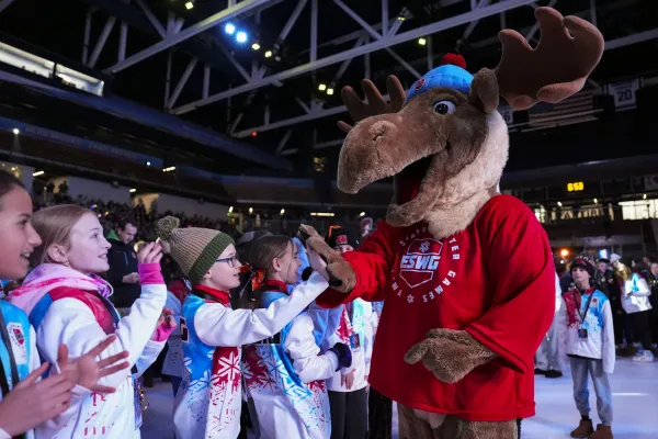 A group of children in colorful winter jackets high-five a person in a cheerful moose mascot costume.