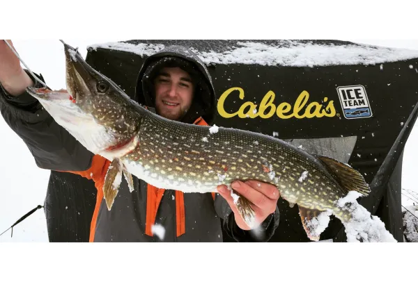A pike held up high in front of the ice fishing tent.