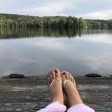 Two feet in flip flops next to a water as smooth as glass.