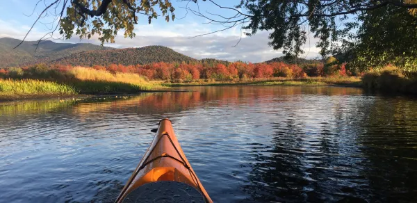 A tip of a kayak matches the fall foliage on the far side of the lake.