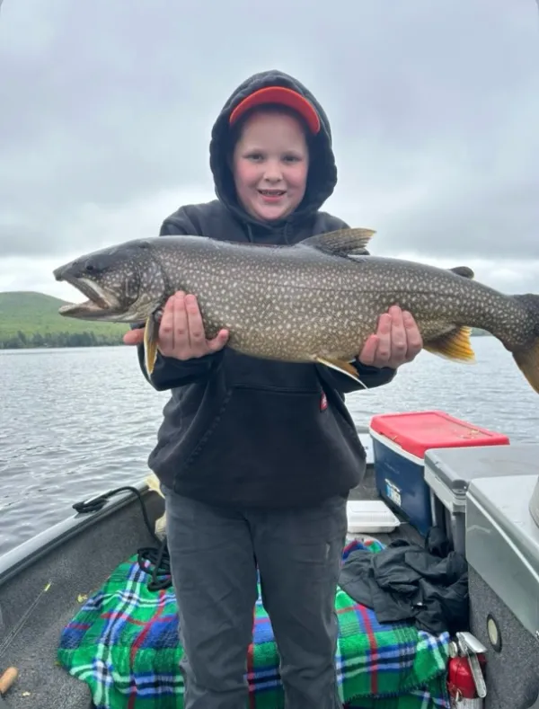 A smiling kid standing on a boat holding a large fish.