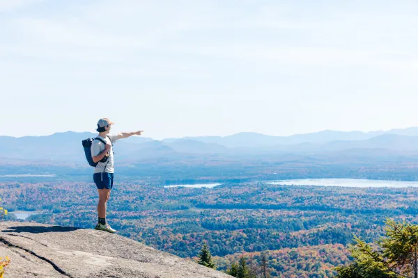 A man points to a mountain range covered in foliage in the fall.