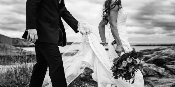 Groom holds the train of the bride's gown.