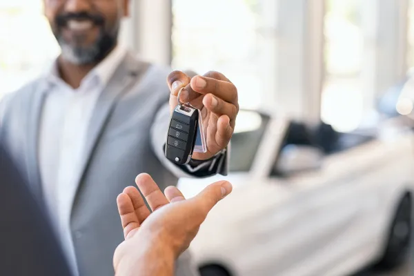 A man in a suit hands a set of car keys to an outstretched hand.