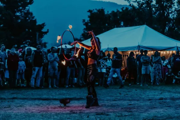 Fire dancer seen twirling flaming batons at music festival at dusk