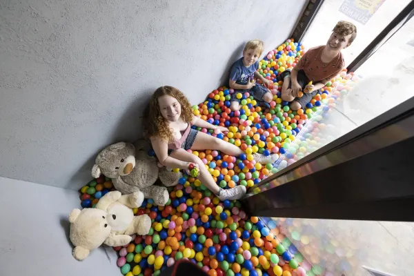 Kids smiling and playing in a colorful ball pit by windows