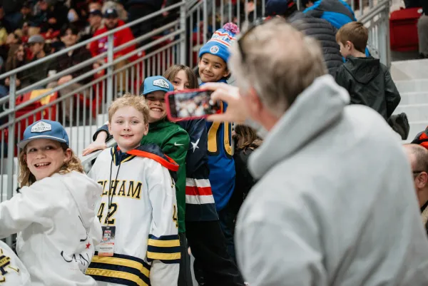 Older man takes photo of kids in hockey jerseys in crowd at hockey game in 1980 Herb Brooks Arena