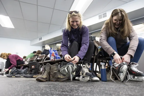 People putting on ice skates and leaving piles of shoes under chairs.