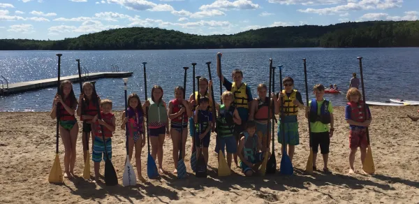 A group of young paddlers stand with their life jackets on the sandy beach