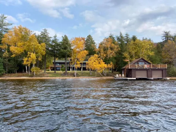 A view of the Alpenglow Lakeside Lodge with prominent boathouse from in the water in early fall when the birches turn yellow.