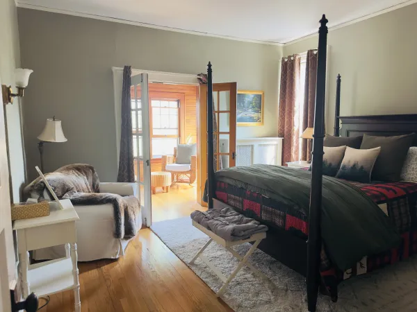 A dark 4 post bed with adirondack themed bedding and bright french doors calling you through.