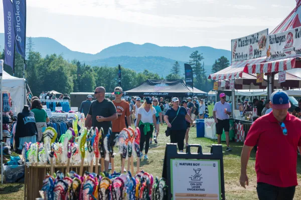 People mill around food and lacrosse gear vendors at Lake Placid Summit Lacrosse Tournament with mountains in background