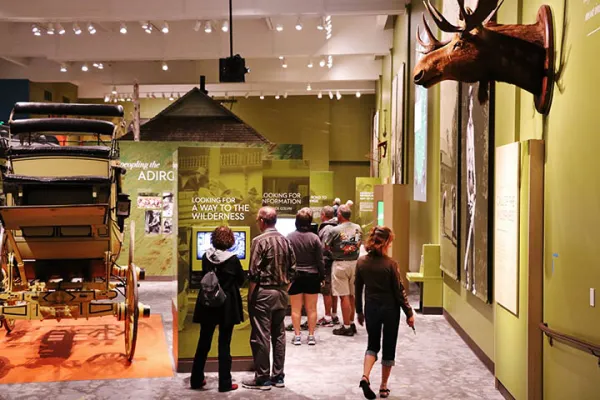A large room with green walls where people are viewing the plaques under various displays like a carriage and a moose.