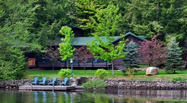 The cottage from the water with adirondack style chairs on the dock.