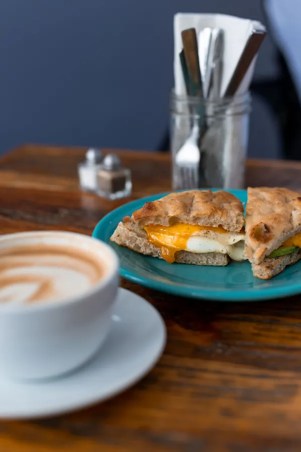 Egg sandwich on a fluffy english muffin next to a latte.