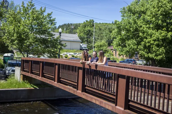 Three girls rest and soak up the view on the bridge along the Saranac Lake Riverwalk.