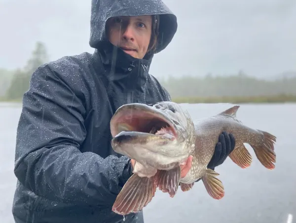 A man in a rain coat holds a fish.