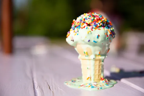 A close-up of a melting ice cream cone with sprinkles on a lavender table.