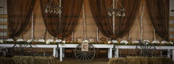 Head table with large wagon wheel and swooping curtains.