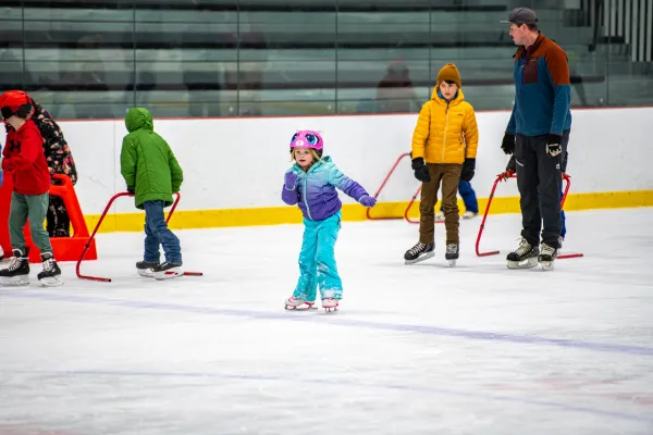 A child in a bright outfit skates without training bar while other still use them in the background.