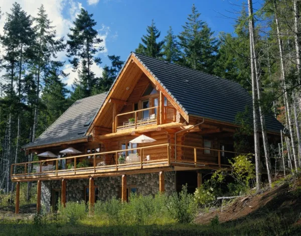 The exterior of a three story log cabin with wrap around deck and balcony above 
