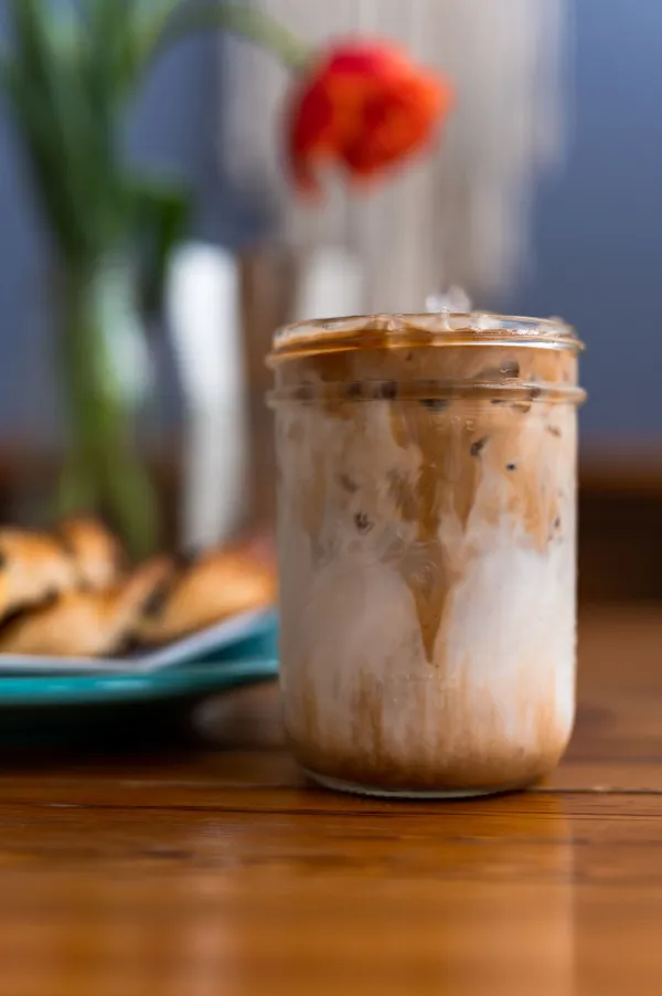 An iced coffee in a mason jar next to breakfast on a plate.