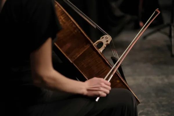 Person in black sits while holding cello in one hand an a bow in the other