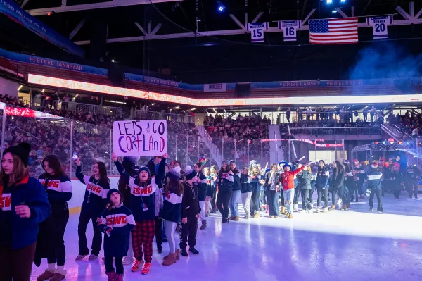 A large group of athletes wearing "ESWG" sweaters parades across the ice during an opening ceremony.