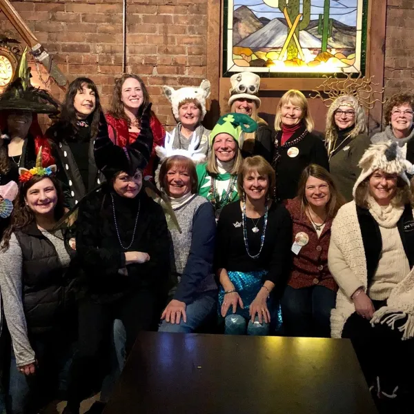 A group of smiling women wearing silly hats and carnival beads