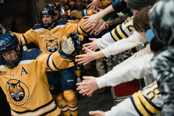 Quinnipiac hockey players high five hands hanging over partition as they leave the ice of the 1980 Herb Brooks Arena