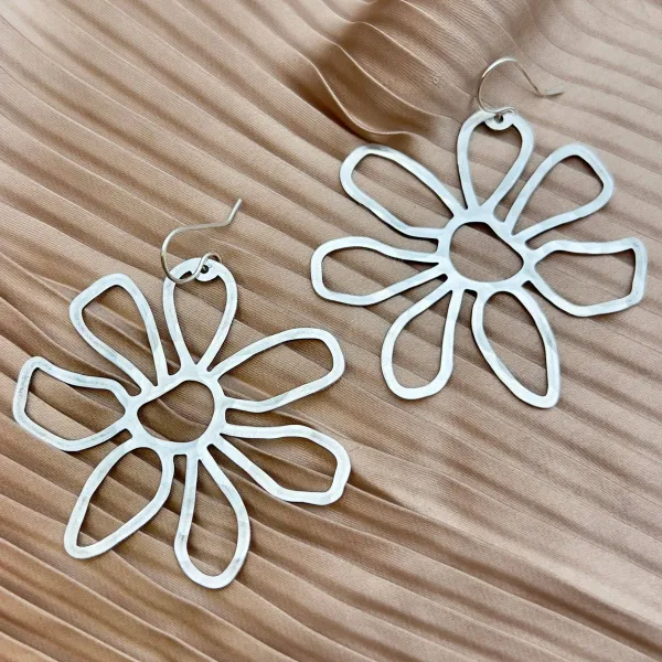 Silver colored dangling earrings of hammered metal shaped like daisies.