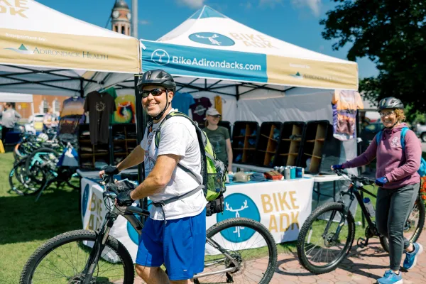 smiling man on bike with vendor tent in the background 