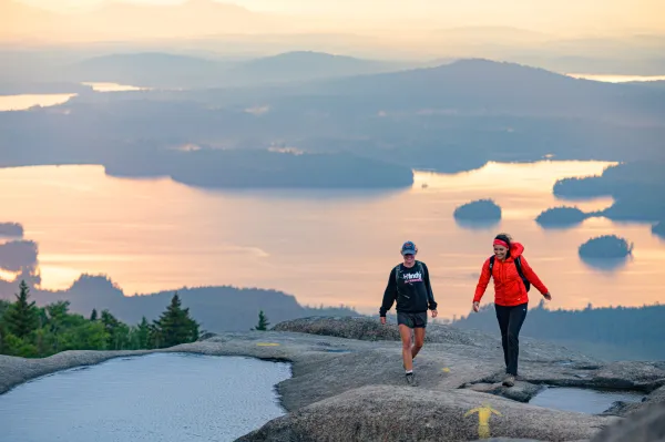 A couple people hiking Ampersand Mountain, a bare rock summit.