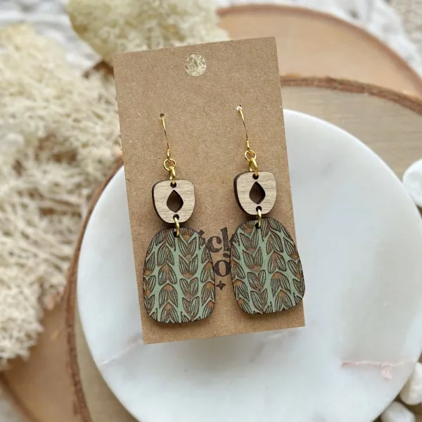 Birch bark dangling earrings with a teal green chalk wash and a repeating pattern of carved hearts.