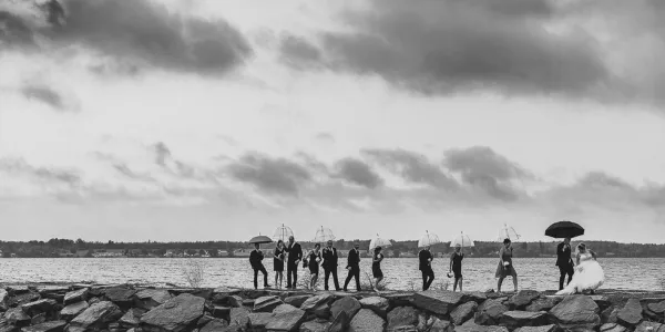 Wedding party stand on the rocks by the water.