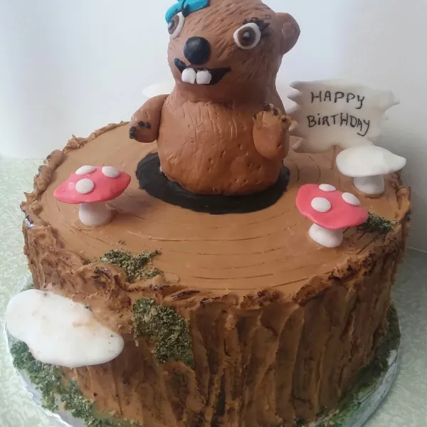 A birthday cake decorated like a log with a flag, woodland creature and mushrooms.