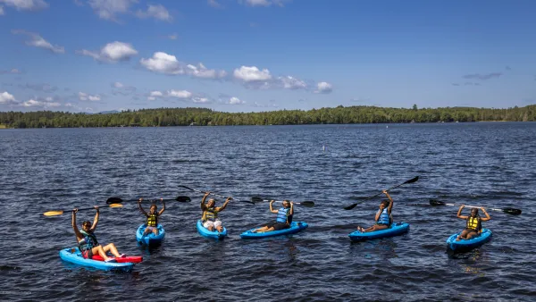 A group of kayakers hold their paddles above their heads in triumph.