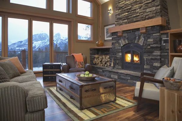 The main living space of a large home with two stories of windows, a stone fireplace with built in wood storage and ample lush seating. 