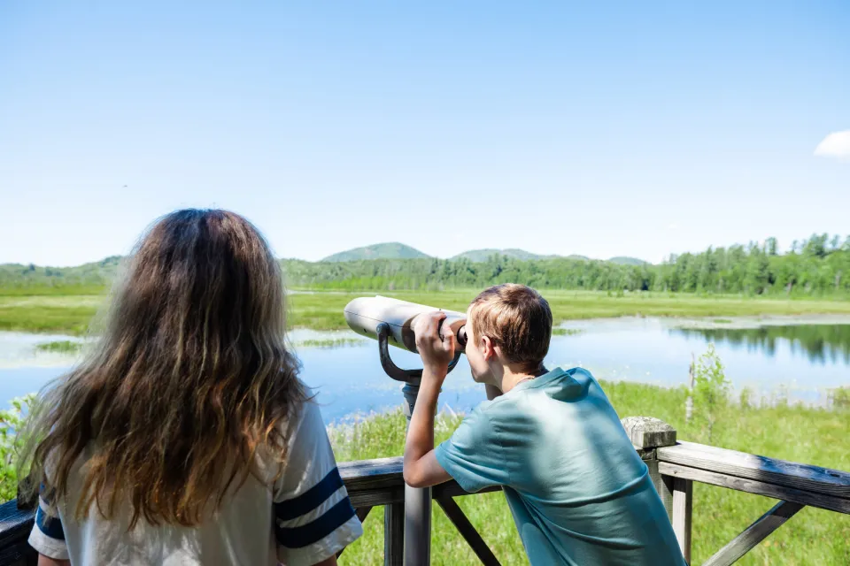 A young boy looks through binoculars on a nature trail. 